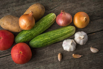 Garlic, onion, cucumber, potatoes and tomato on an old table