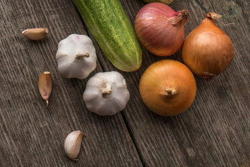 Garlic, onion, cucumber, potatoes and tomato on an old table