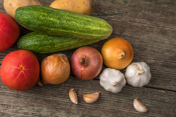 Garlic, onion, cucumber, potatoes and tomato on an old table