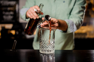 Bartender making red alcoholic cocktail , metal jigger and bar environment