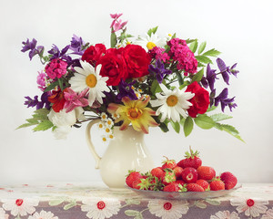 Bouquet of garden flowers in a jug and strawberries.