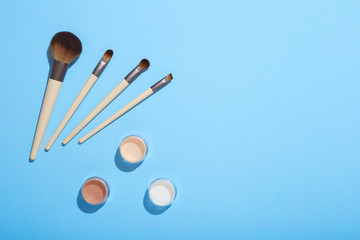 Set of makeup brushes and mineral eye shadows on blue background