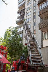Firefighters climb the fire escape to extinguish fire on the upper floors of residential building.