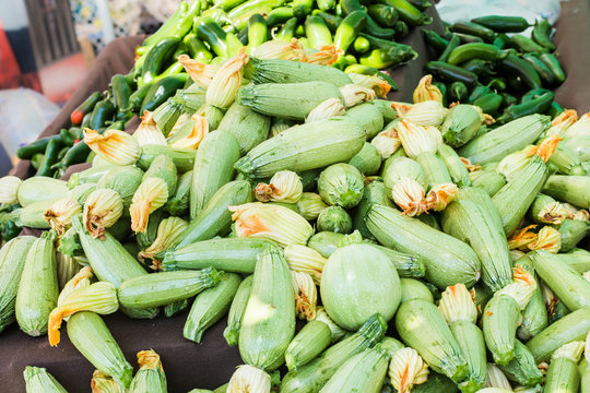 Squash piled high at farmers market fruit stand with green peppers in the background. Fresh vegetables for sale.