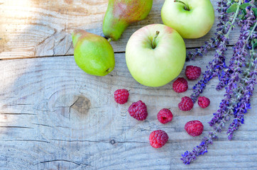 apples and pears and raspberries lie near field with purple flowers on a wooden Board
