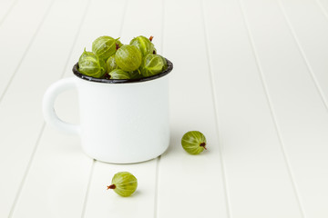 Fresh green gooseberries in an enamel mug on white table