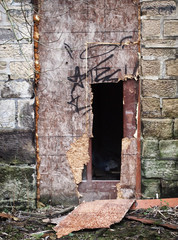 broken boarded up vandalized door in an abandoned derelict stone building