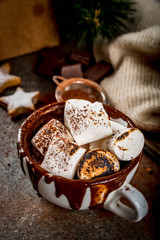 Fototapeta na wymiar New Year and Christmas treats. Traditional sweets. A cup of hot chocolate with marshmallow fried on fire, gingerbread stars, with sweater on black stone background, copy space