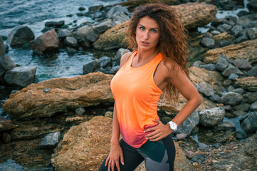 Beautiful girl sportsman posing on the beach before running. Woman athlete on the background of the sea.