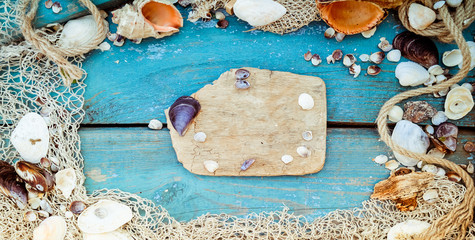 Summer vacation relaxation background theme with seashells, fishing net, rope, stones and weathered wood blue background with copy space. Vintage toning. Wide photo