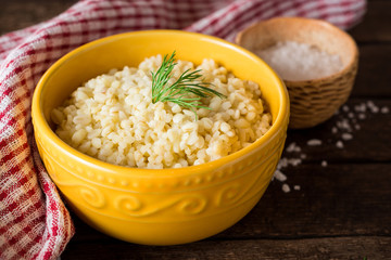 Bulgur with dill in yellow ceramic bowl on dark wooden background