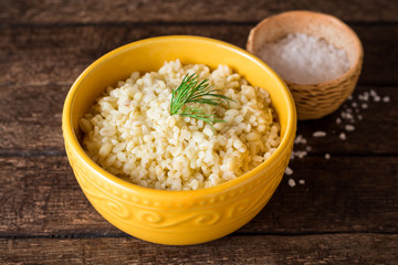 Bulgur with dill in yellow ceramic bowl on dark wooden background