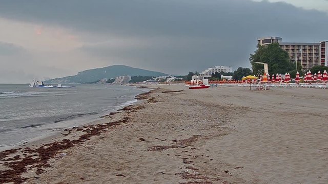 The Black Sea shore from Albena, Bulgaria with golden sands, sunrise, blue fresh water, sunbeds and umbrellas near beach hotels, coast with houses and fluffy clouds sky