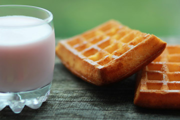 Glass of raspberry yogurt and two freshly baked wafers on old grey wooden table against blurred green background