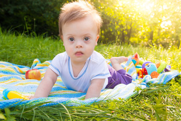 Portrait of Cute baby boy with Down syndrome lying on blanket in summer day on nature
