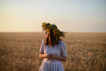 beautiful girl in wreath of flowers in meadow on sunny day. Portrait of Young beautiful woman...