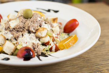 Tuna salad with lettuce, olives, and tomatoes. Orange decoration on a white plate.