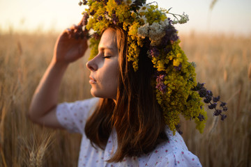 beautiful girl in wreath of flowers in meadow on sunny day. Portrait of Young beautiful woman wearing a wreath of wild flowers. Young pagan Slavic girl conduct ceremony on Midsummer. Earth Day