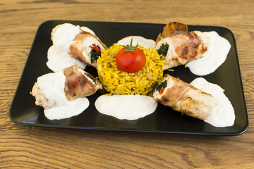 Roasted chicken breast rolls wrapped in bacon slices, served with rice, cherry tomato and toping on the side. Beautifully served plate at the restaurant.