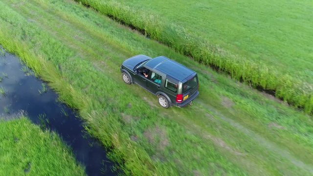 Aerial footage offroad SUV sport utility vehicle driving fast over green grassland in between two straight canals off-road truck driving fast in straight direction followed by UAV drone 4k quality