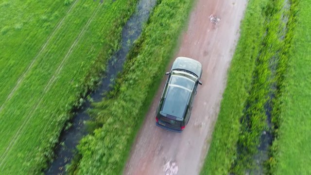 Aerial top-down view following offroad SUV sport utility vehicle driving fast over unpaved gravel road in between two straight canals off-road truck driving fast in straight direction followed by UAV