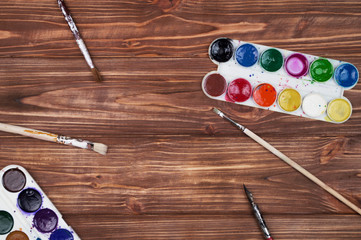 Artist tools over wooden table. Art brushes, watercolor paint tubes, artist palette on wood