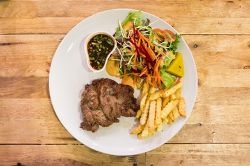 Top view of pork pepper steak with vegetable and french fries and sauce in white plate on wooden table.