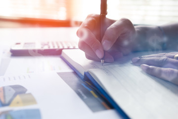 Businessman writing on notebook on wooden table, People are recording accounting data calculated from a calculator.Concept finance planing and analyzes management.