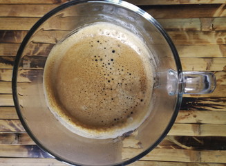  Enjoy morning coffee today with popular hot beverage menu,espresso coffee with golden fine-bubbled crema seen from above in crystal clear cup on bamboo plate.