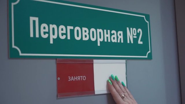 Unrecognisable female hand moves plate from free to occupied on door with green plastic sign cyrillic text meeting room