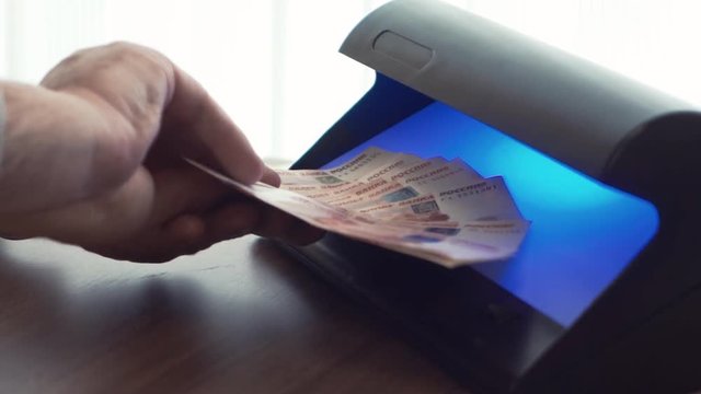 Unrecognisable businessman hand in wool jacket checking five thousand ruble banknote on uv light detector in office, close up
