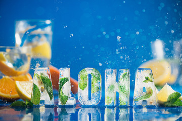 Ice cube lettering with frozen mint leaves, lemon slices and oranges on a blue background with...