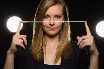 Young caucasian woman conductor poses with baton in a dark space with stage lights