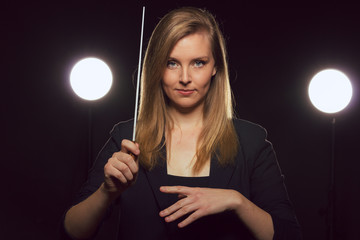 Young caucasian woman conductor poses with baton in a dark space with stage lights