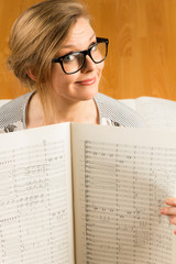 Young caucasian hipster woman with glasses with music shirt sits on sheet music in a room