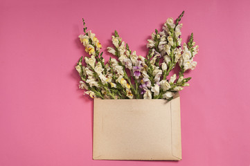Flowers composition. Heart shaped flowers in envelope on pink background. Flat lay, top view.