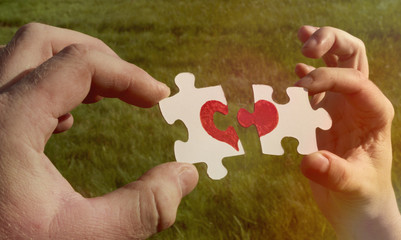 Two cardboard puzzles with a painted red heart are held in the hands on a background of green grass. l compound.