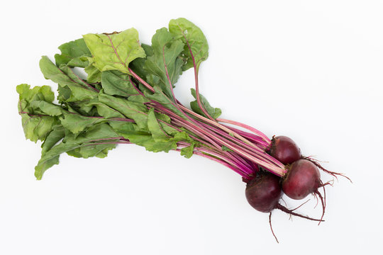 Three freshly picked beets with the greens photographed on a white background.