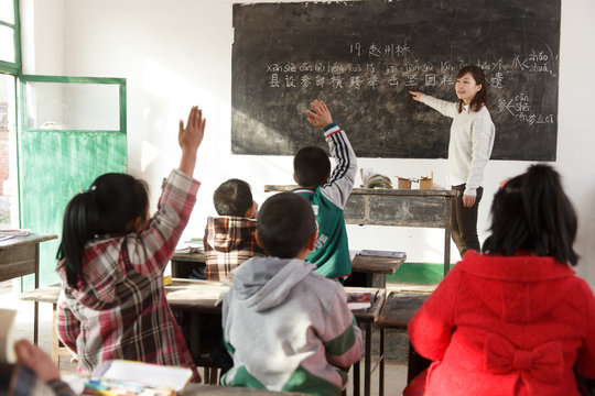 Teacher pointing at blackboard with Chinese script in classroom