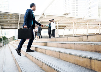 Lifestyle of young Asian businessman holding black business briefcase walking up the stair with...