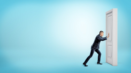 A small businessman pushes a closed door on a white wooden door frame.