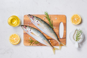Fish dish cooking with various ingredients. Fresh raw fish decorated with lemon slices and herbs on wooden table.