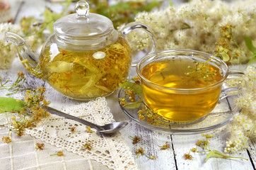 Glass cup of transparent tea and pot with linden flowers on the napkin