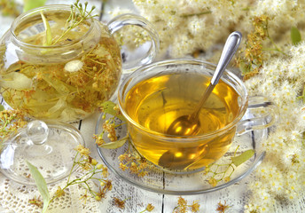 Cup of linden tea with spoon and linden flowers on wooden planks