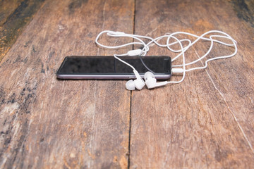 white earphone on mobile phone with table old wooden vintage background and copy space select focus with shallow depth of field