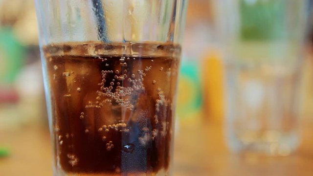 Cinemagraph of bubble bubbling in glass with cola and ice on a table