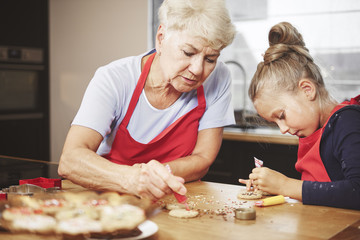 Grandma with girl baking and decorating cookies together - obrazy, fototapety, plakaty