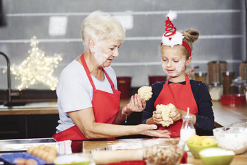 Senior with girl kneading dough in kitchen .
