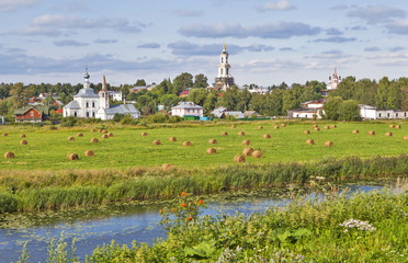 Пейзаж поля со рулонами сена и река Каменка на фоне достопримечательностей Суздаля. Владимирская область. Золотое Кольцо. Россия
