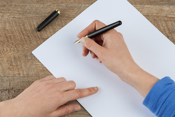 Woman hands holding fountain pen and blank piece of paper on wooden table